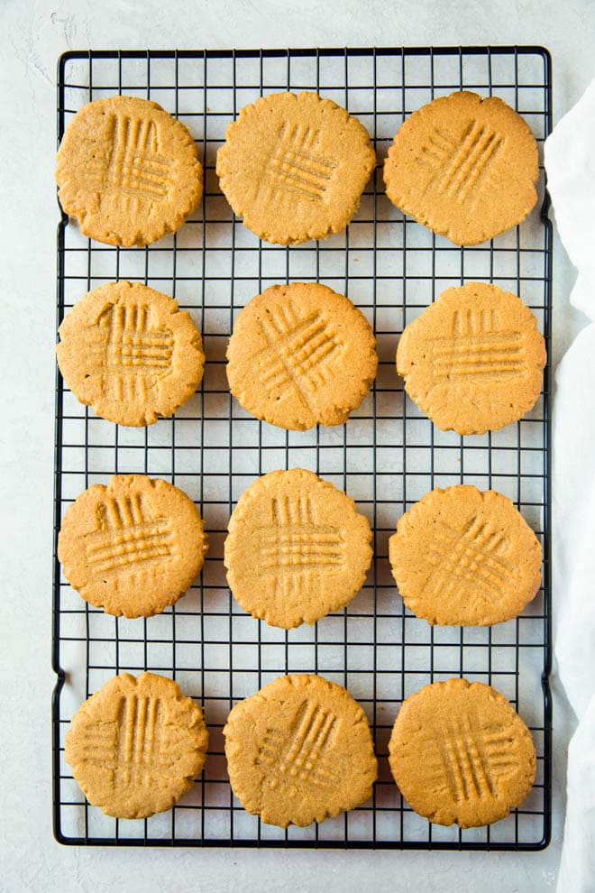 une douzaine de biscuits au beurre de cacahuètes posés sur une grille de refroidissement sur un comptoir blanc
