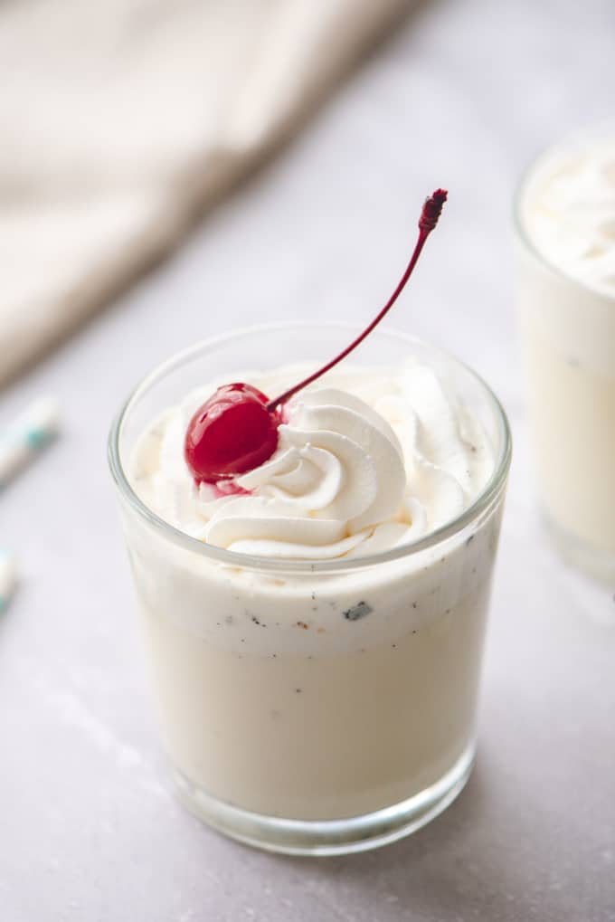 Verre rempli d'une boisson lactée tres leches à la vanille. Garni de crème fouettée et d'une cerise.