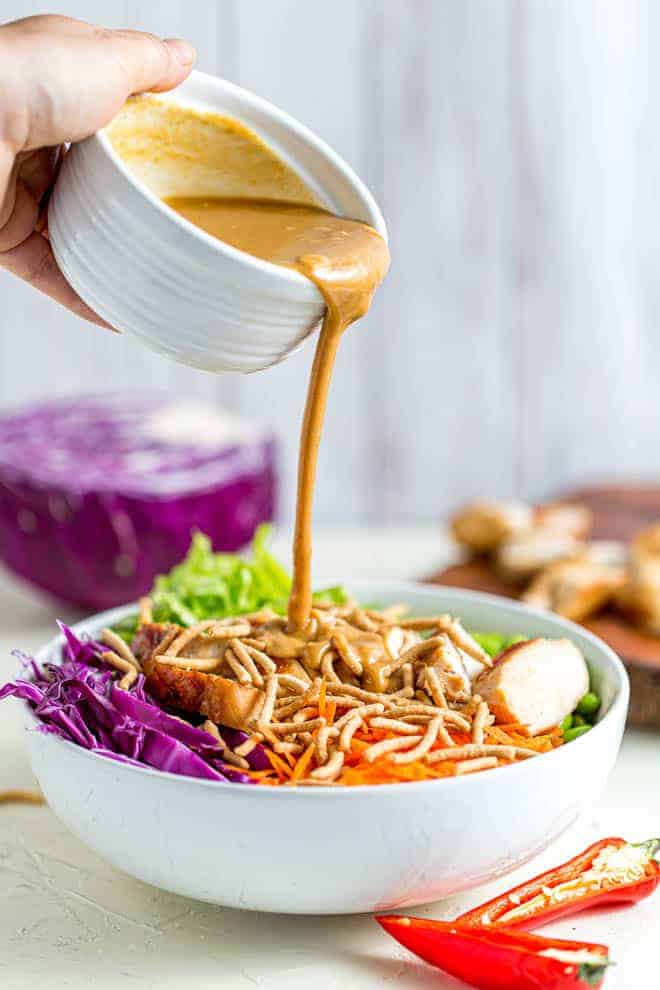 Verser de la sauce aux cacahuètes dans un bol de salade de poulet thaï.
