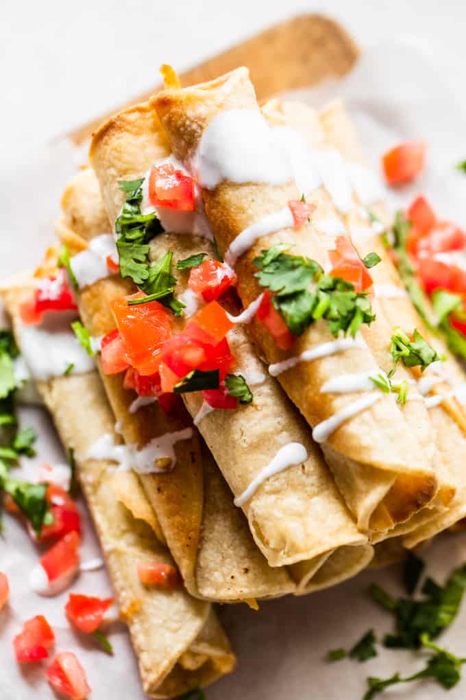 Vue aérienne de taquitos empilés, arrosés de crème, de tomates en dés et de coriandre.