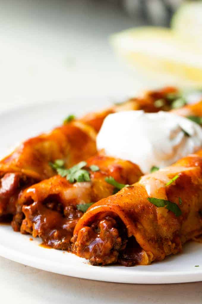 Enchiladas de bœuf maison servies sur une assiette avec de la coriandre coupée en dés et un tourbillon de crème aigre sur le dessus.