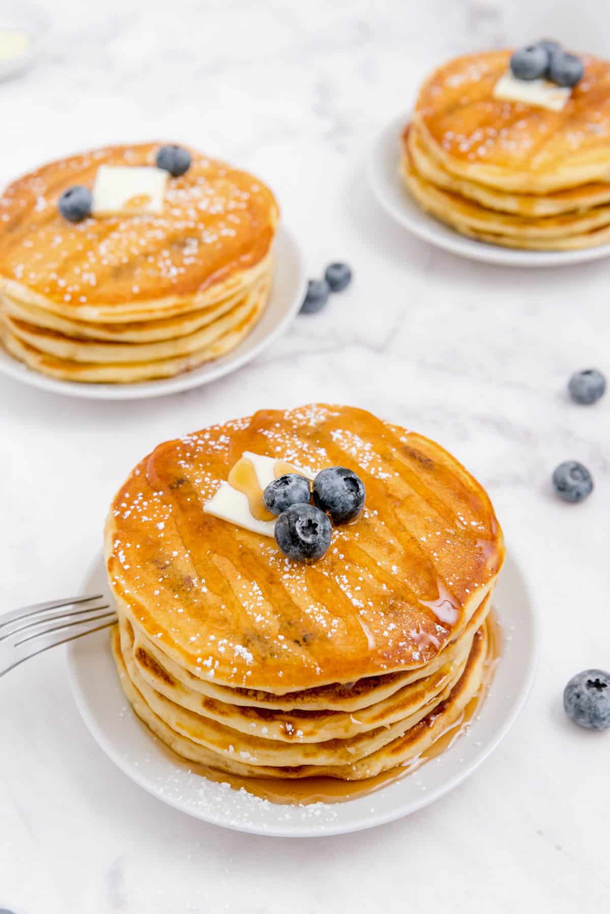 trois piles de crêpes aux myrtilles et au babeurre posées sur des assiettes blanches sur un comptoir