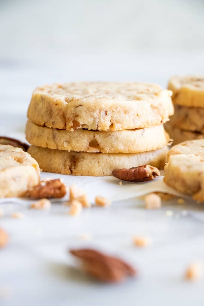 Une pile de biscuits sablés au beurre et aux noix de pécan avec des morceaux de noix de pécan et des morceaux de caramel.