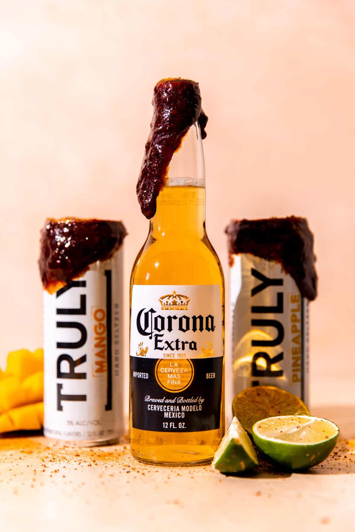 Une bouteille de Corona et deux seltzers durs avec une pâte de chamoy de couleur foncée sur le dessus, saupoudrée de tajin.