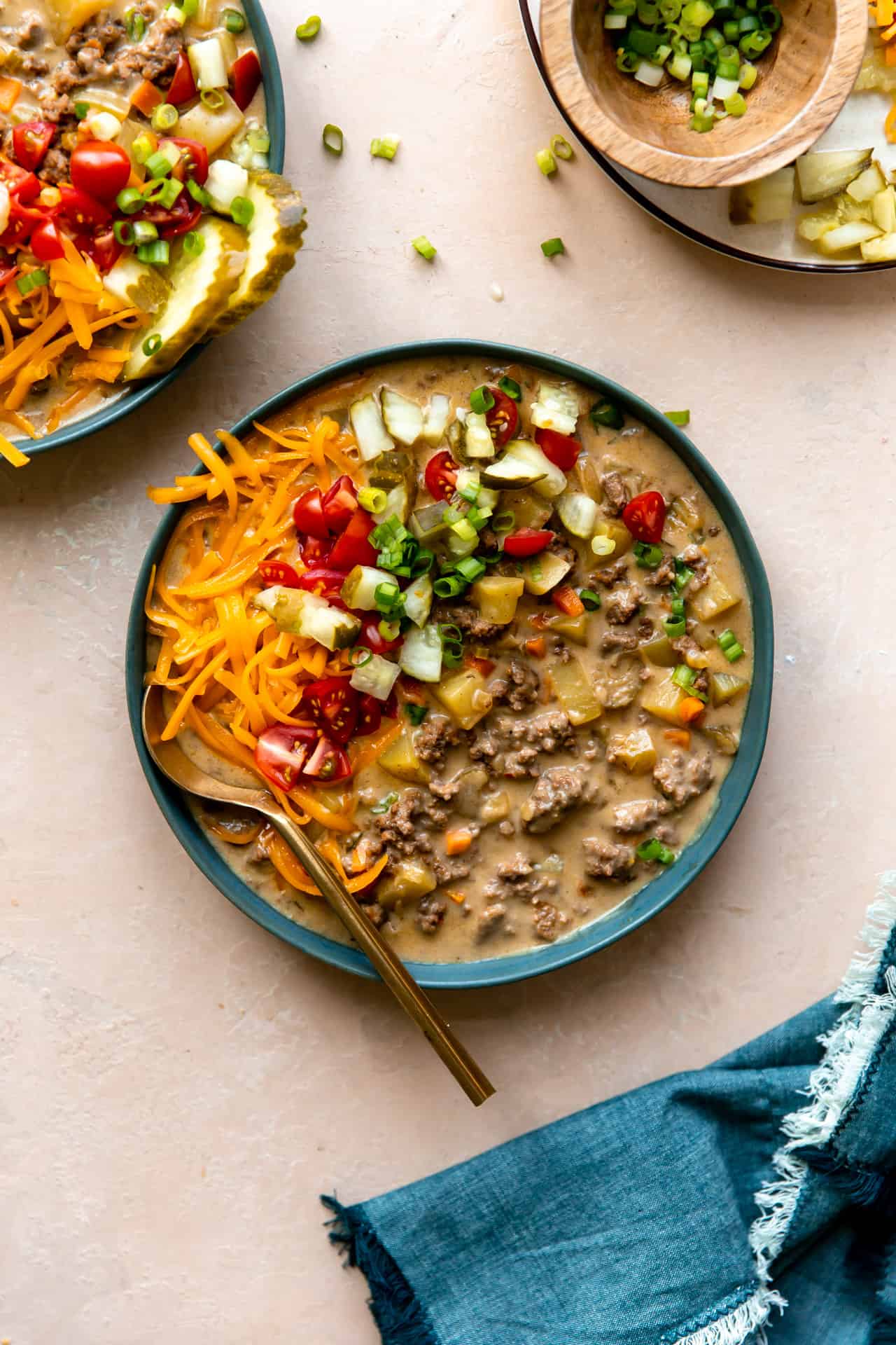 Bol rempli de soupe au cheeseburger et garni de tomates en dés, de cornichons, de fromage et d'herbes.