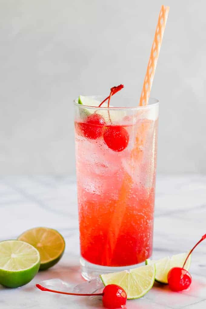 Verre rempli de Cherry Limeade, garni de cerises au marasquin et d'un quartier de citron vert.