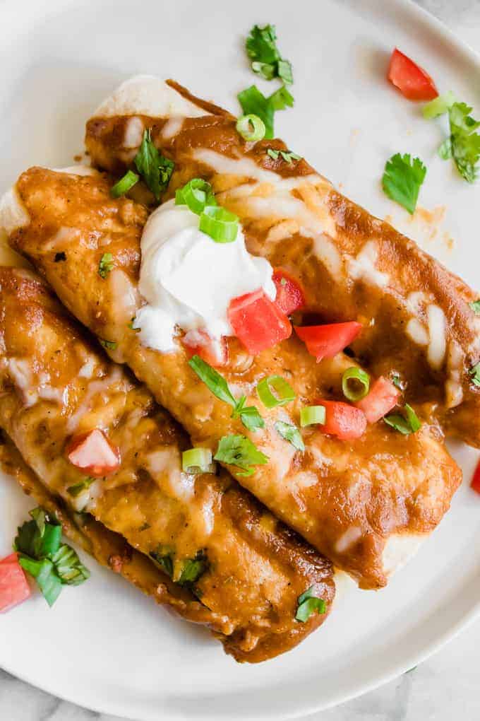 Vue aérienne de trois enchiladas au chorizo sur une assiette garnie de crème aigre, de coriandre et de tomates.