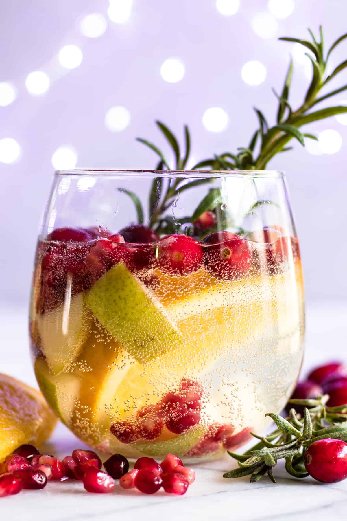 Verre rempli d'une sangria blanche de Noël garnie de romarin.