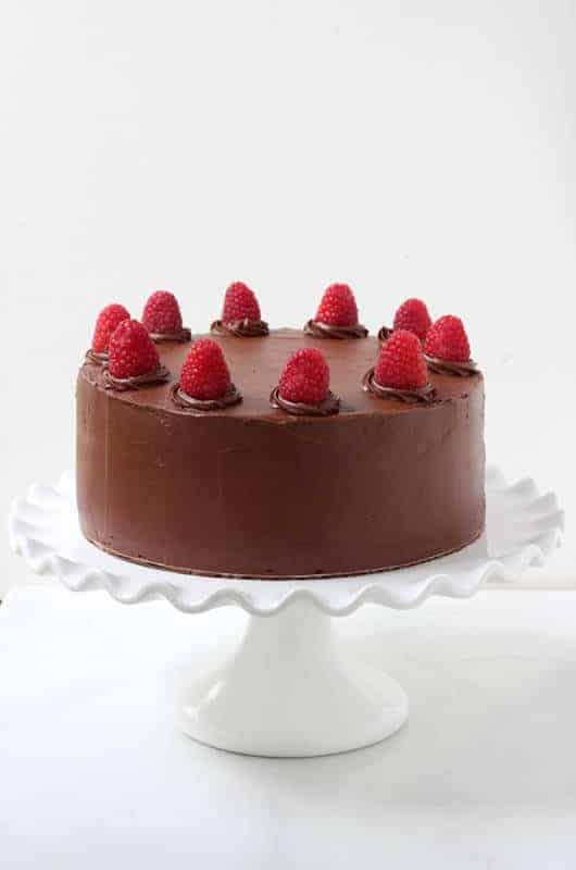 Gâteau au chocolat surmonté de framboises fraîches, posé sur un plateau à gâteau blanc.