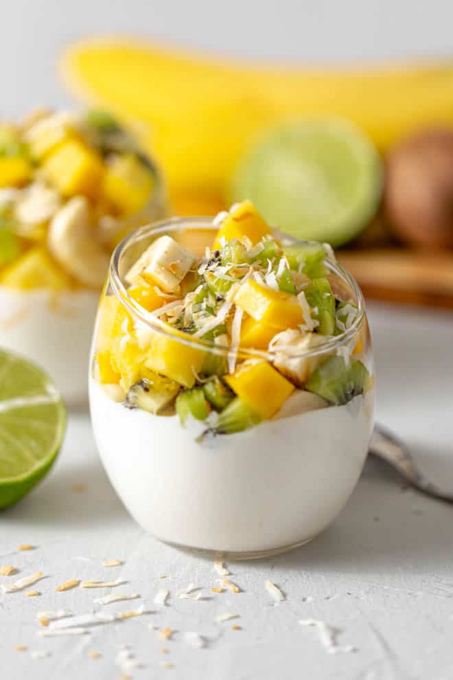 pot en verre transparent rempli de yogourt grec avec des morceaux de mangue, de kiwi, de banane et d'ananas empilés sur le dessus