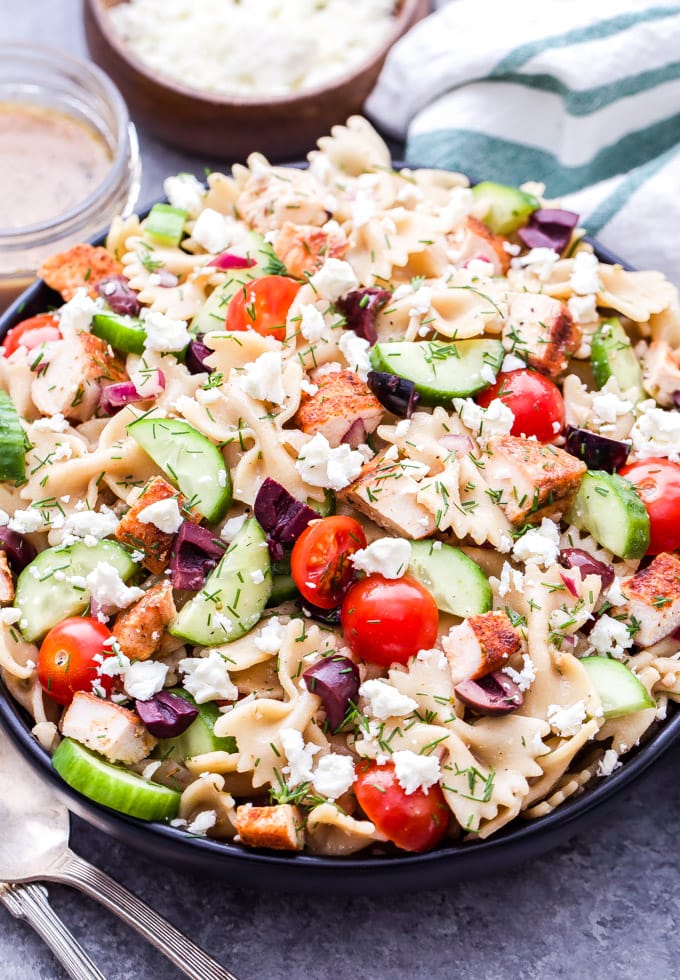 un bol rempli de pâtes, de poulet, de concombres, de tomates, d'olives et d'autres ingrédients pour préparer une salade grecque de pâtes au poulet