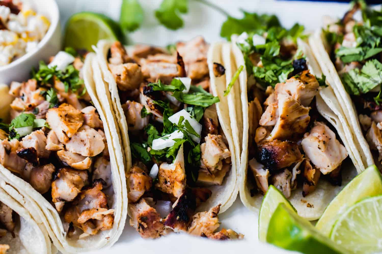 Tacos de poulet grillé disposés les uns à côté des autres avec des quartiers de citron vert sur le côté.