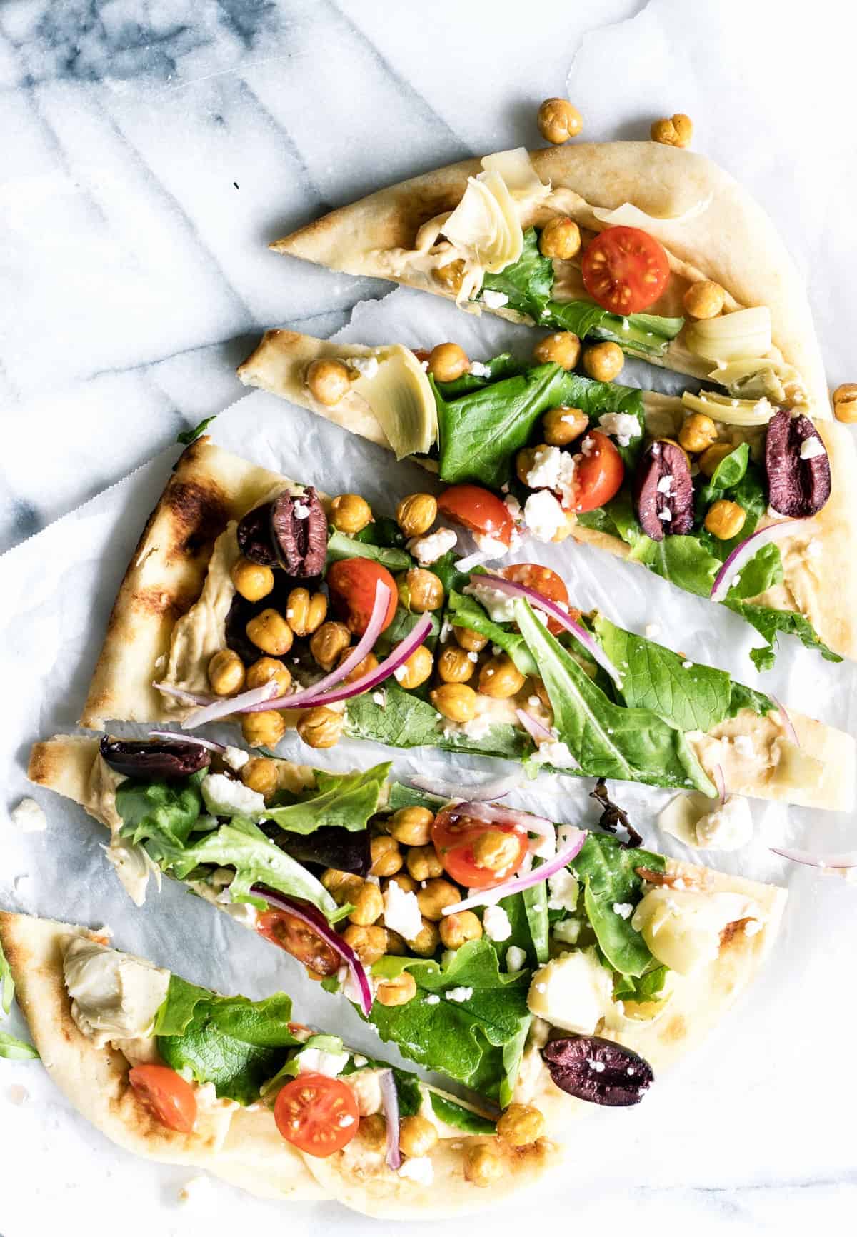 Gros plan sur une pizza de pain plat tranchée, recouverte d'houmous et de garnitures.