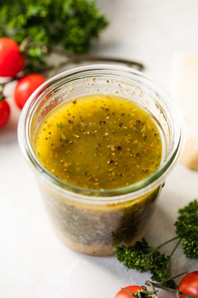 Bocal rempli de vinaigrette italienne maison, avec des tomates sur le côté et du persil frais.