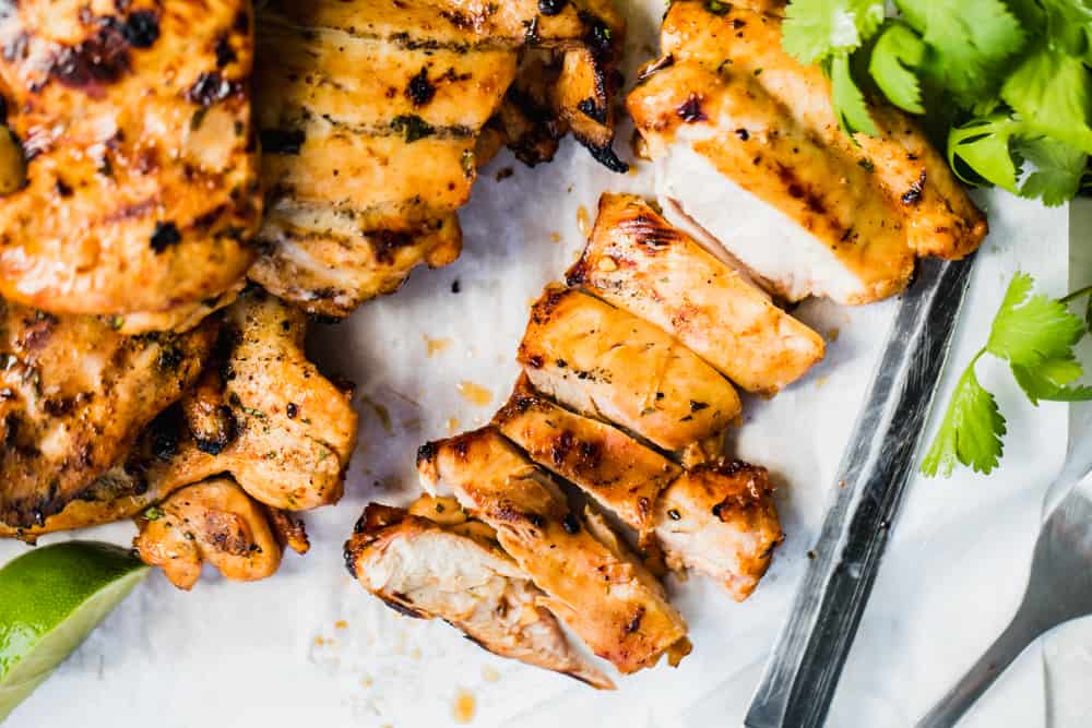 Tranches de poulet grillé mexicain sur une planche à découper avec du papier sulfurisé, de la coriandre et un couteau.