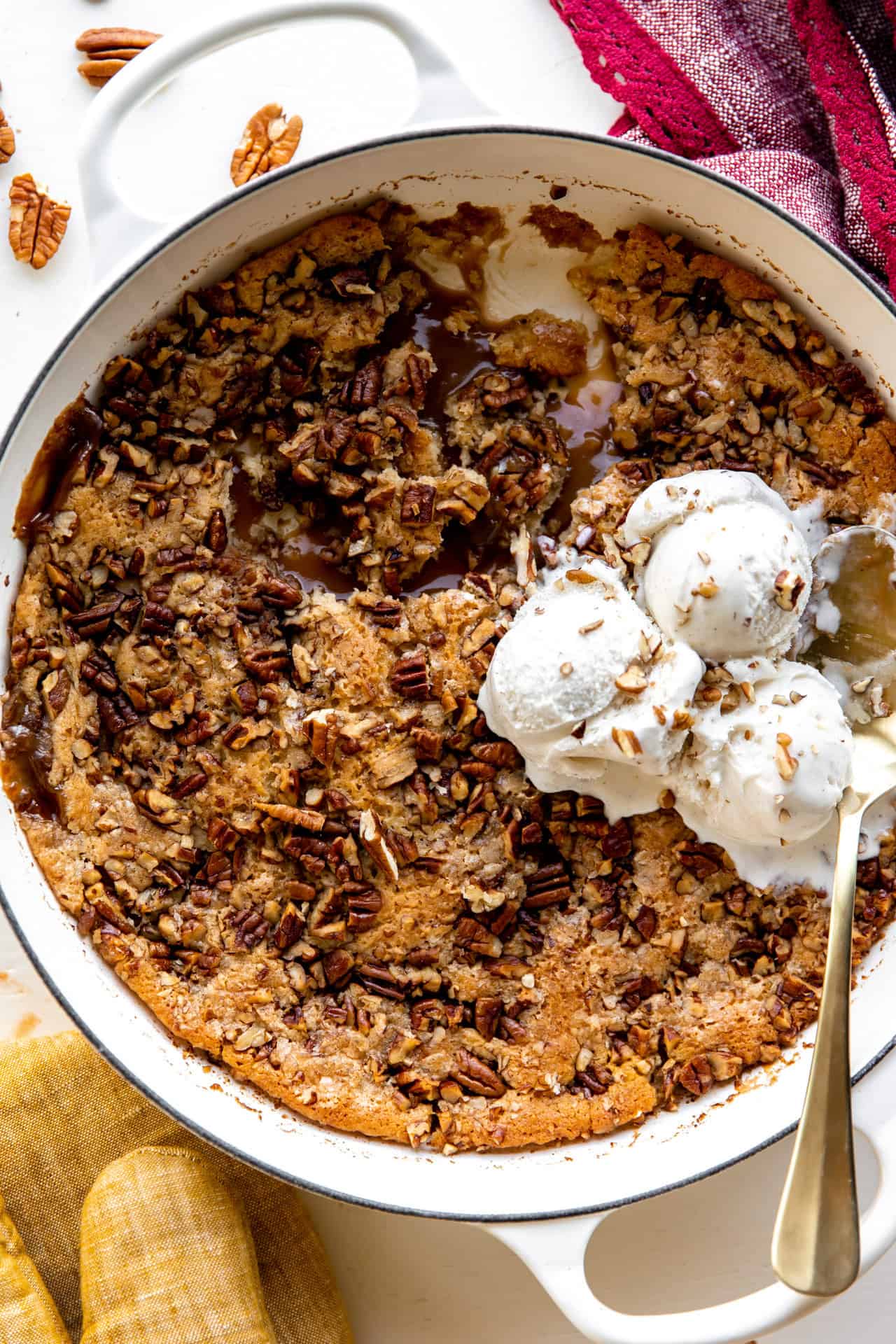 Un plat de cuisson avec un cobbler aux noix de pécan montrant une sauce au caramel et garni de crème glacée.