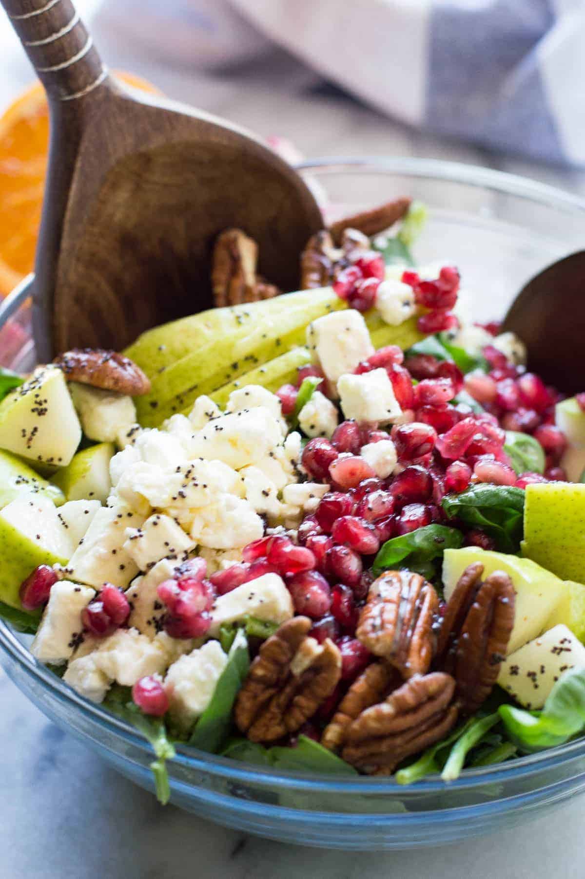 Salade de poires et de grenades avec vinaigrette à l'orange et au pavot. Cette salade est remplie de poires juteuses, de grenades acidulées, de noix de pécan et de feta, le tout sur un lit de jeunes épinards frais et arrosé d'une vinaigrette aux agrumes et à l'orange et aux graines de pavot. Cette magnifique salade sera le clou de n'importe quel repas ! Les couleurs sont parfaites pour les fêtes de fin d'année !