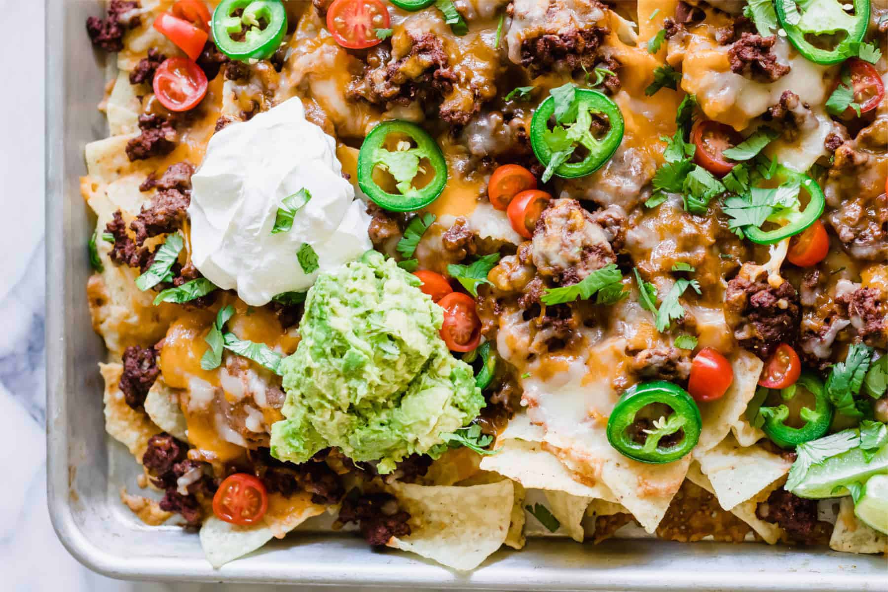 Nachos en feuille avec du bœuf haché, du fromage, des tomates, de la coriandre, des jalapeños, de la crème aigre et du guacamole.