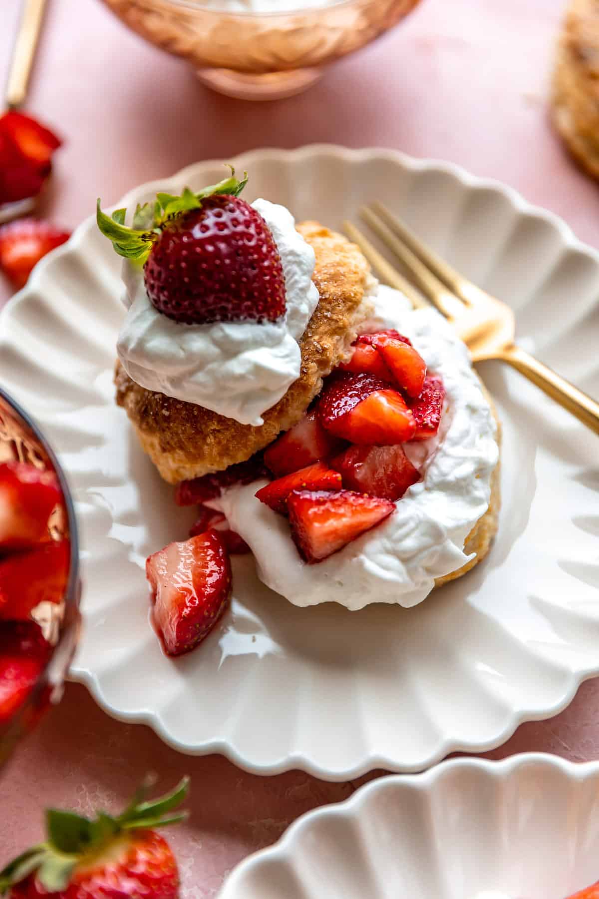 Shortcake aux fraises servi dans une assiette blanche festonnée, fourchette dorée sur le côté.
