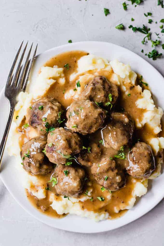 Une assiette remplie de purée de pommes de terre garnie de boulettes de viande et de sauce.