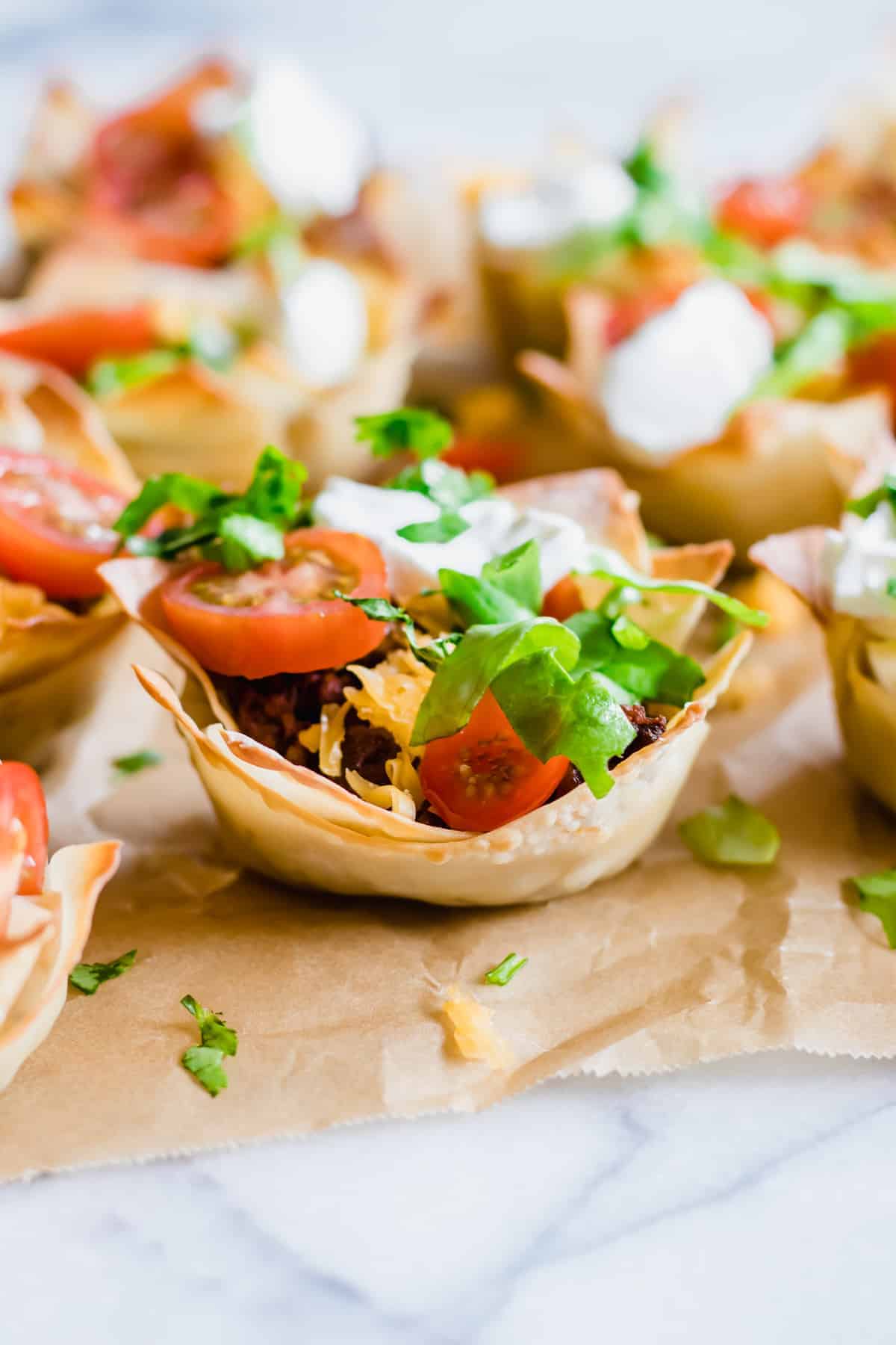 Taco cups. Coupes wonton croustillantes remplies de viande de taco épicée, de fromage fondant, de laitue râpée, de tomates et de coriandre parsemée.