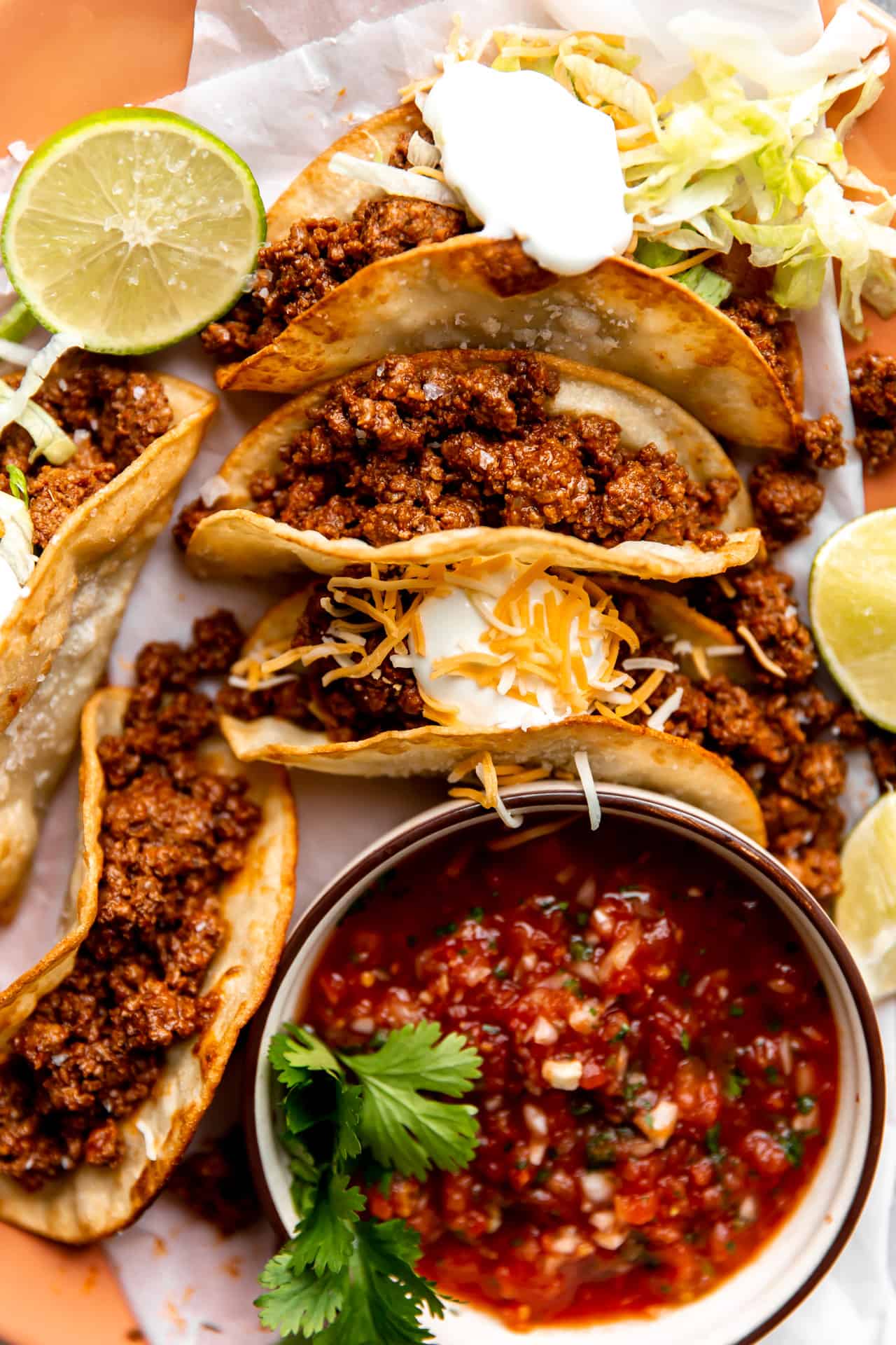 Assiette de tacos de bœuf haché sur des tortillas de maïs frites, garnis de crème aigre et servis avec de la salsa.