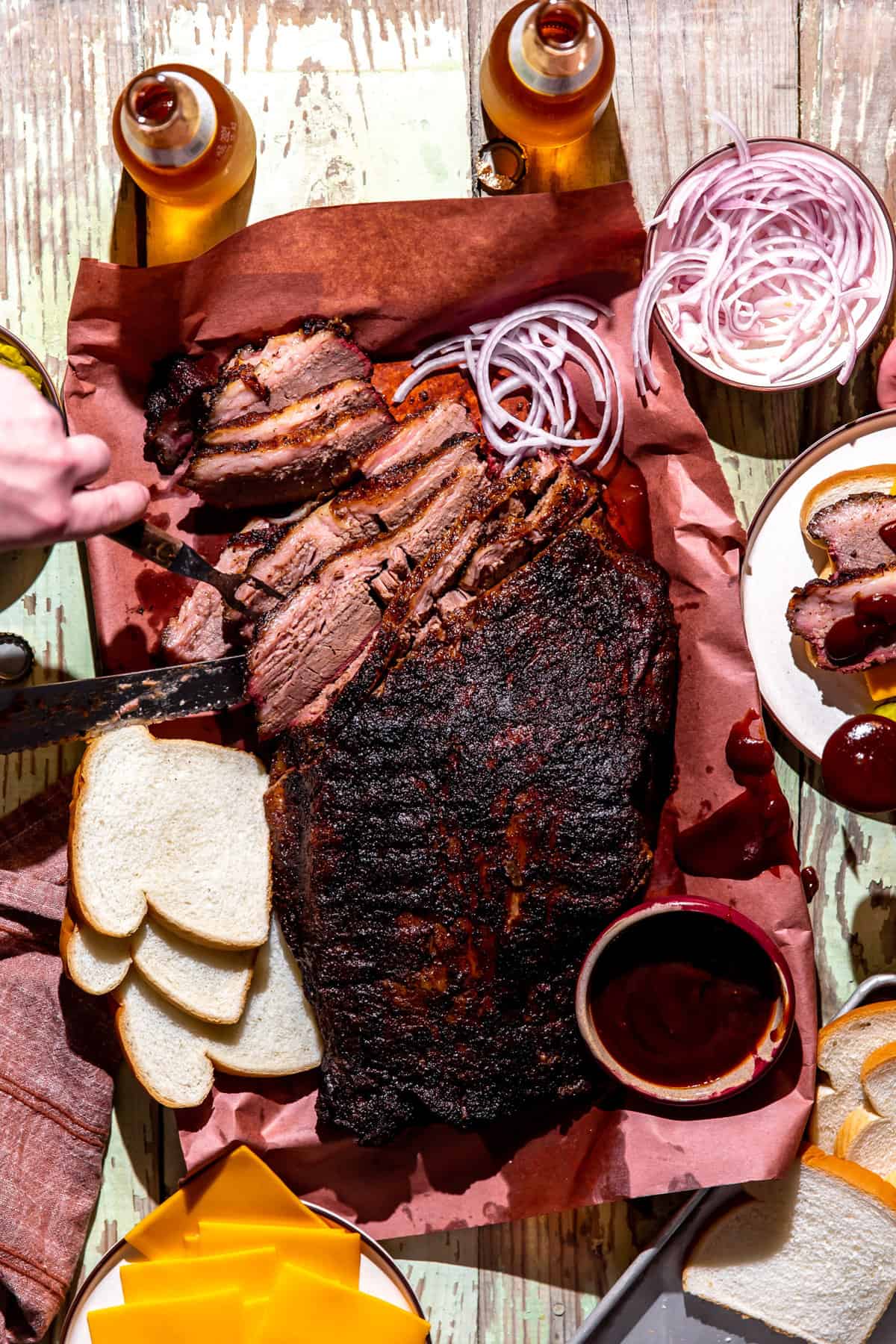 Un barbecue texan à tartiner comprenant une poitrine entière coupée en tranches, entourée de pain blanc, de fromage, d'oignon rouge et de bière.