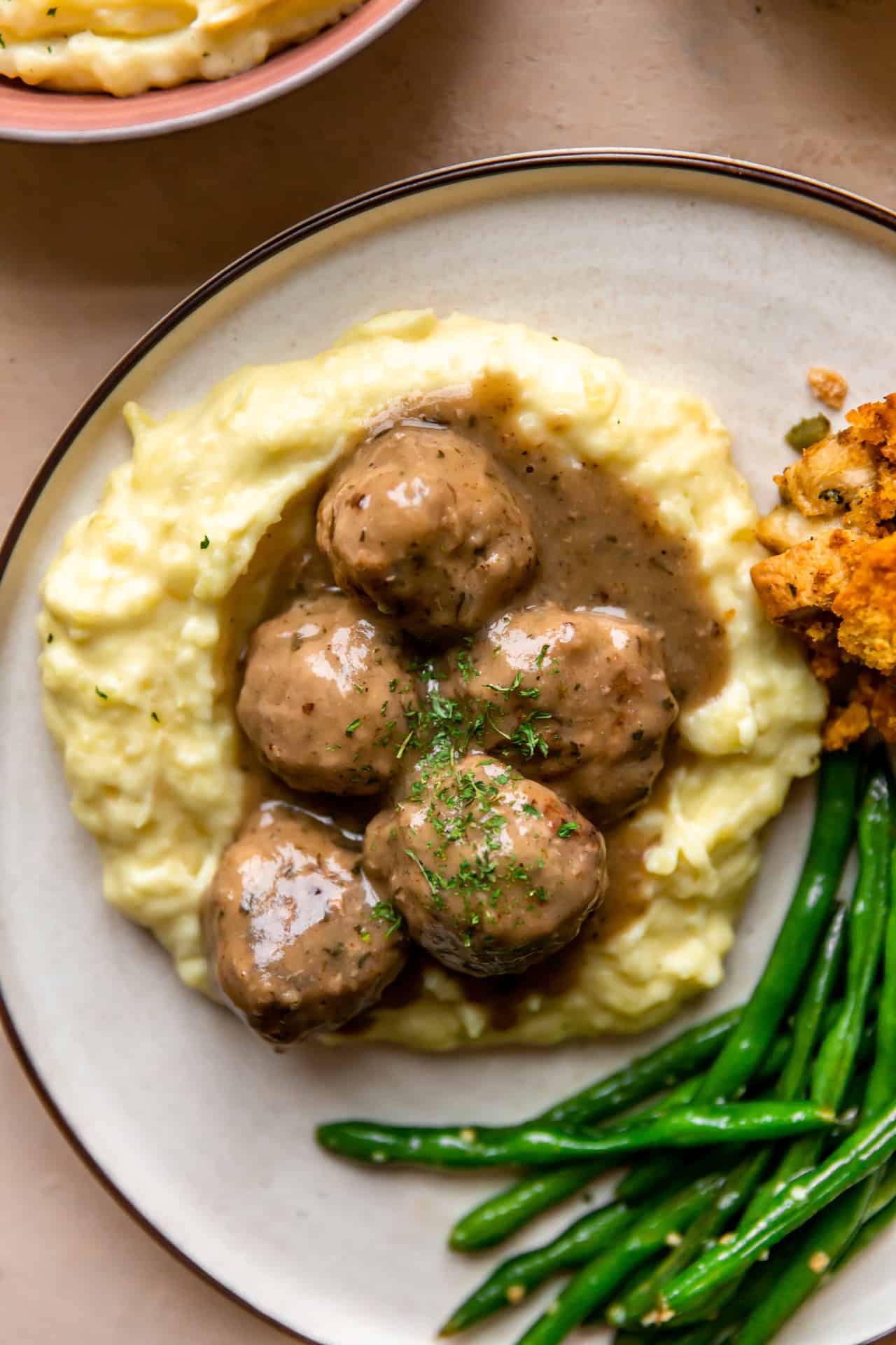 Boulettes de viande de dinde et sauce servies sur de la purée de pommes de terre dans une assiette, avec des haricots verts et de la farce en accompagnement.