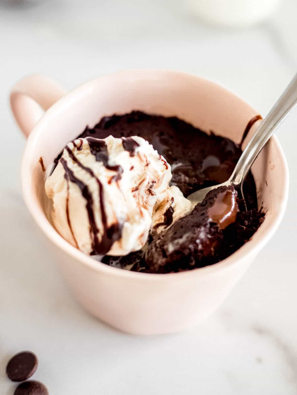 une cuillère dans une tasse avec un brownie au chocolat et une boule de glace à la vanille