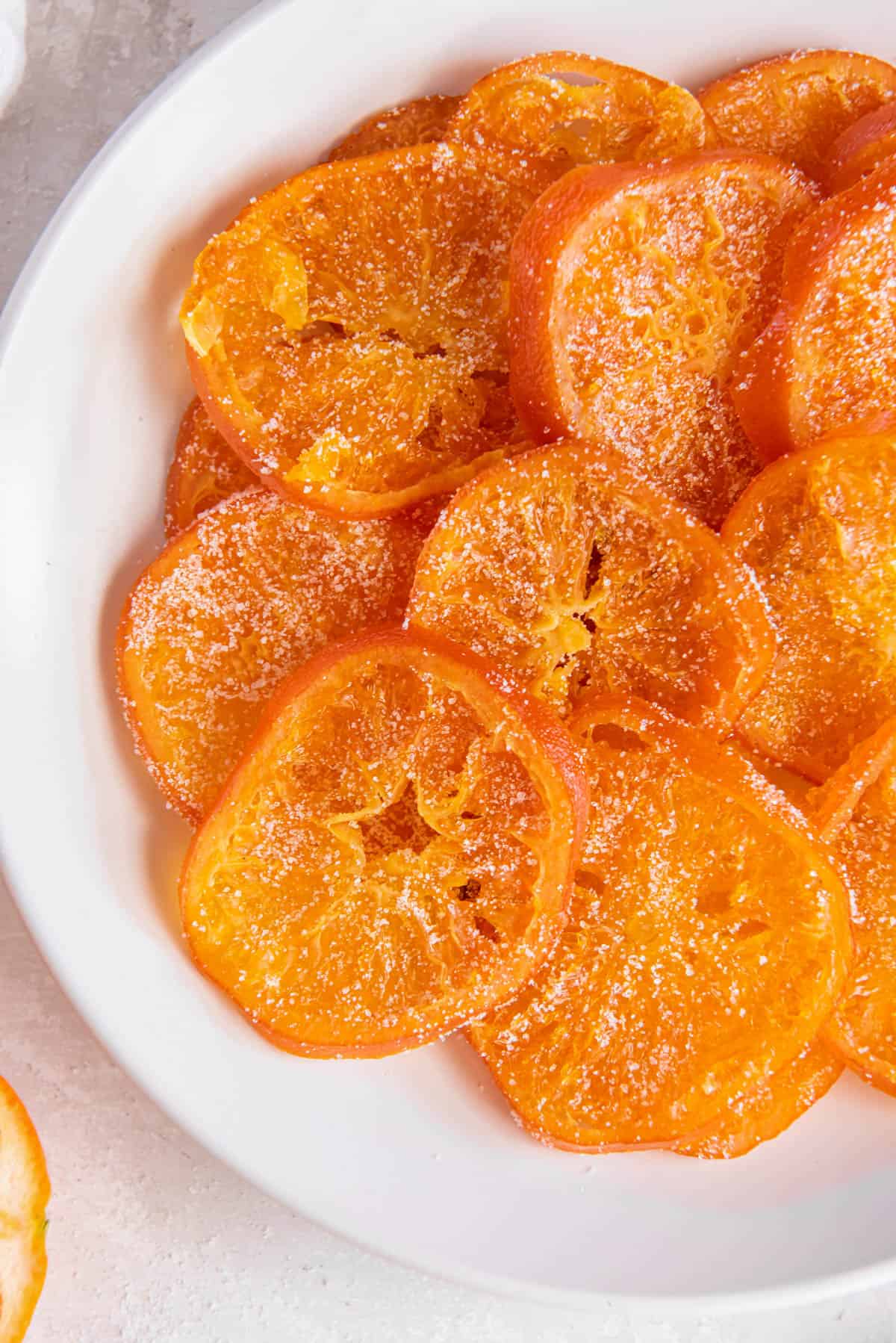 Tranches d'orange confites empilées sur une assiette blanche en forme de cercle.