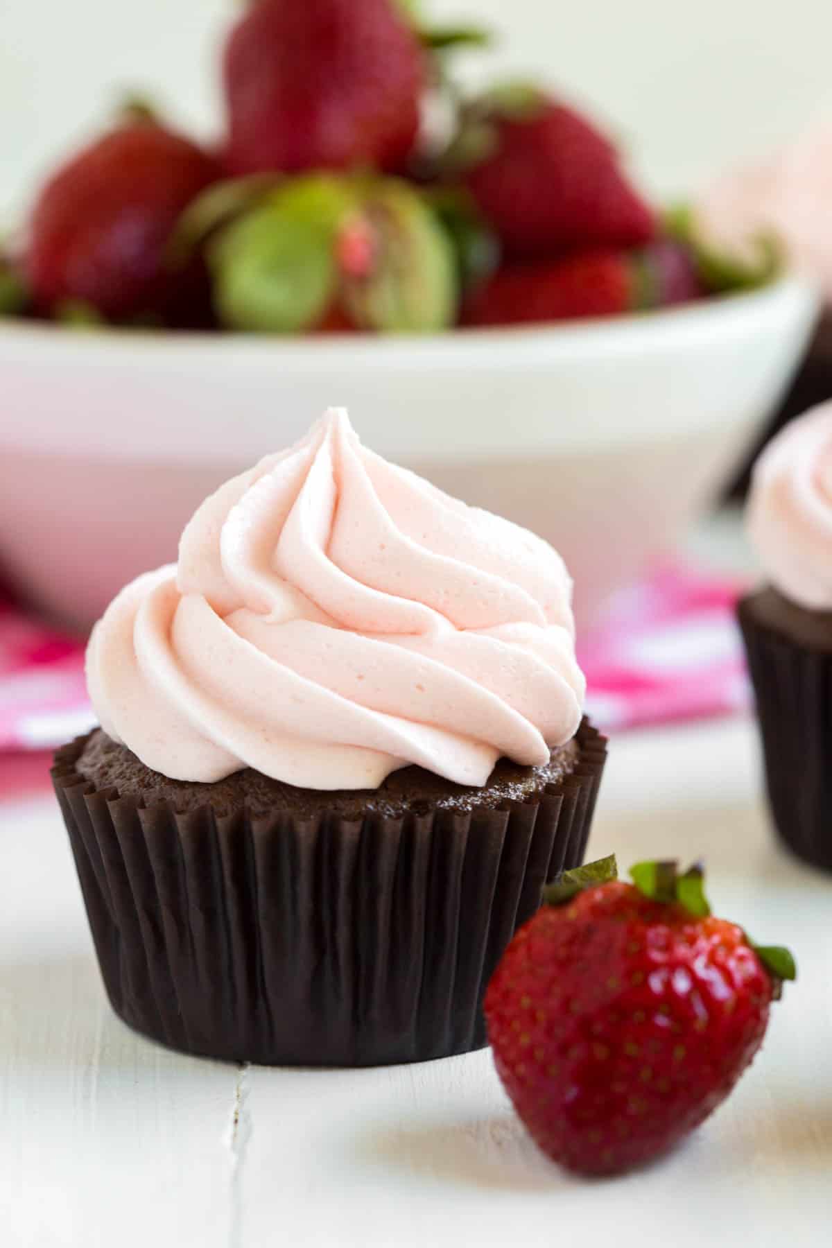 un cupcake au chocolat et à la fraise assis devant un bol de fraises