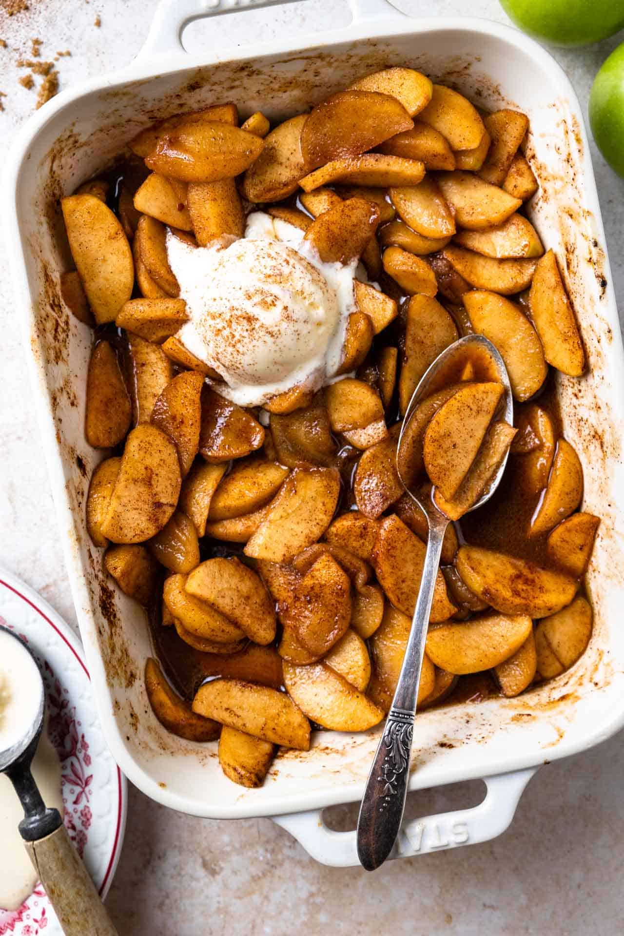 Plat à four rempli de pommes cuites nageant dans un sirop épicé à la cannelle et garni de glace à la vanille.