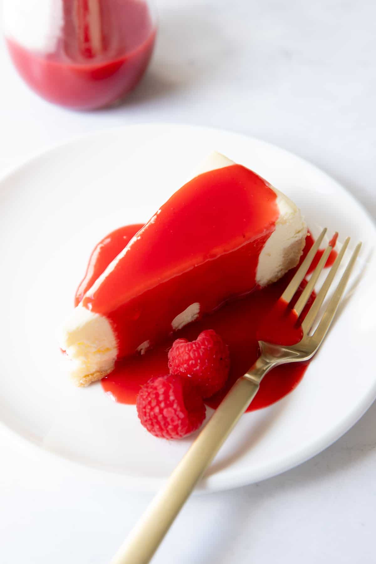 un morceau de cheesecake sur une assiette avec de la sauce framboise dessus