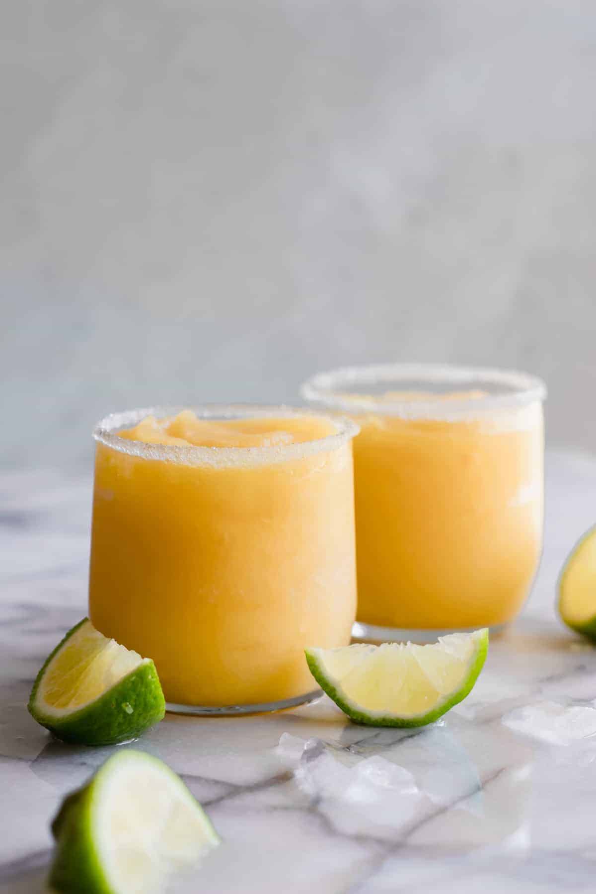 Margarita glacée à la mangue dans un verre bordé de sucre et de quartiers de citron vert.