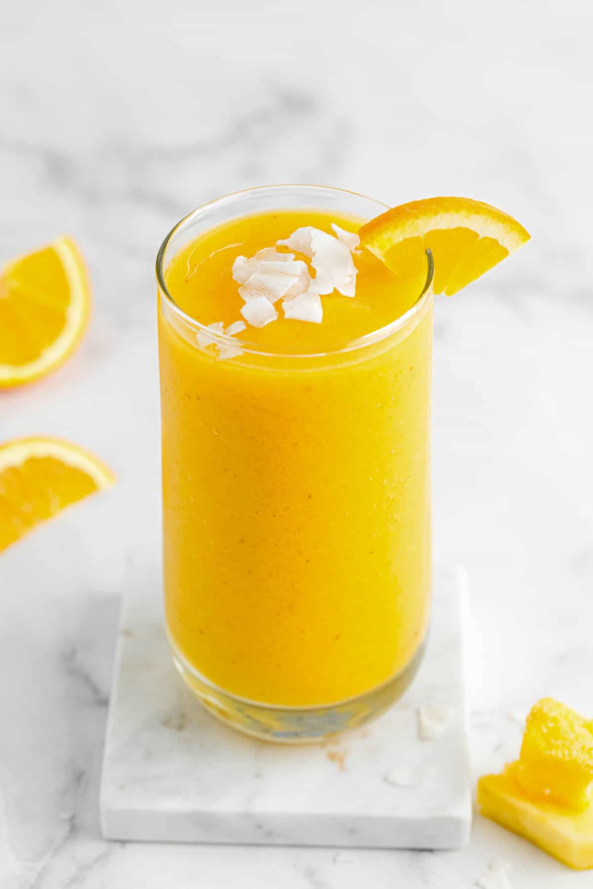 un verre de smoothie aux agrumes avec des flocons de noix de coco et des tranches d'orange sur le dessus