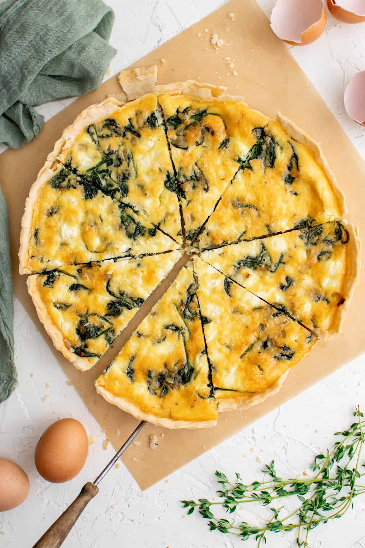 une quiche aux épinards et à la feta coupée en 8 tranches sur une table blanche