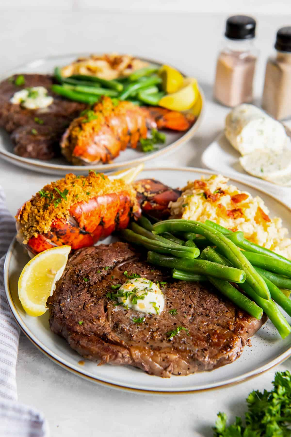 Steak et homard servis sur une assiette avec de la purée de pommes de terre et des haricots verts.