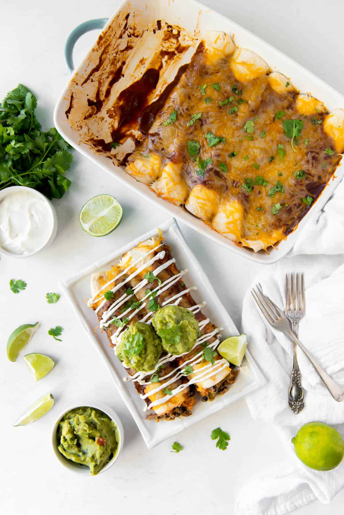 Vue aérienne d'une poêle d'enchiladas aux légumes et d'une assiette contenant deux enchiladas aux légumes, garnies de guacamole et de crème aigre.