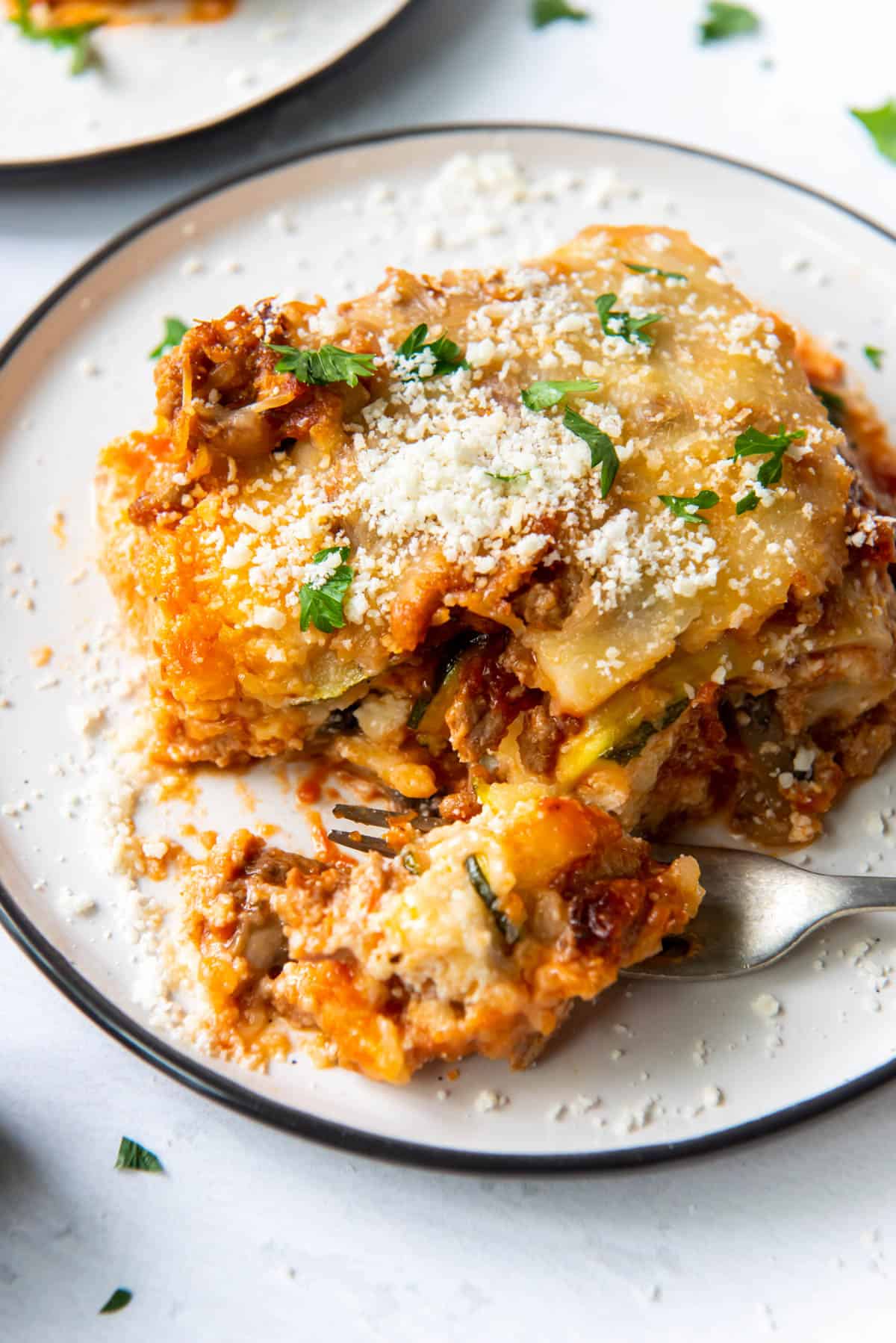 une tranche de lasagne aux courgettes sur une assiette avec une bouchée prélevée à la fourchette